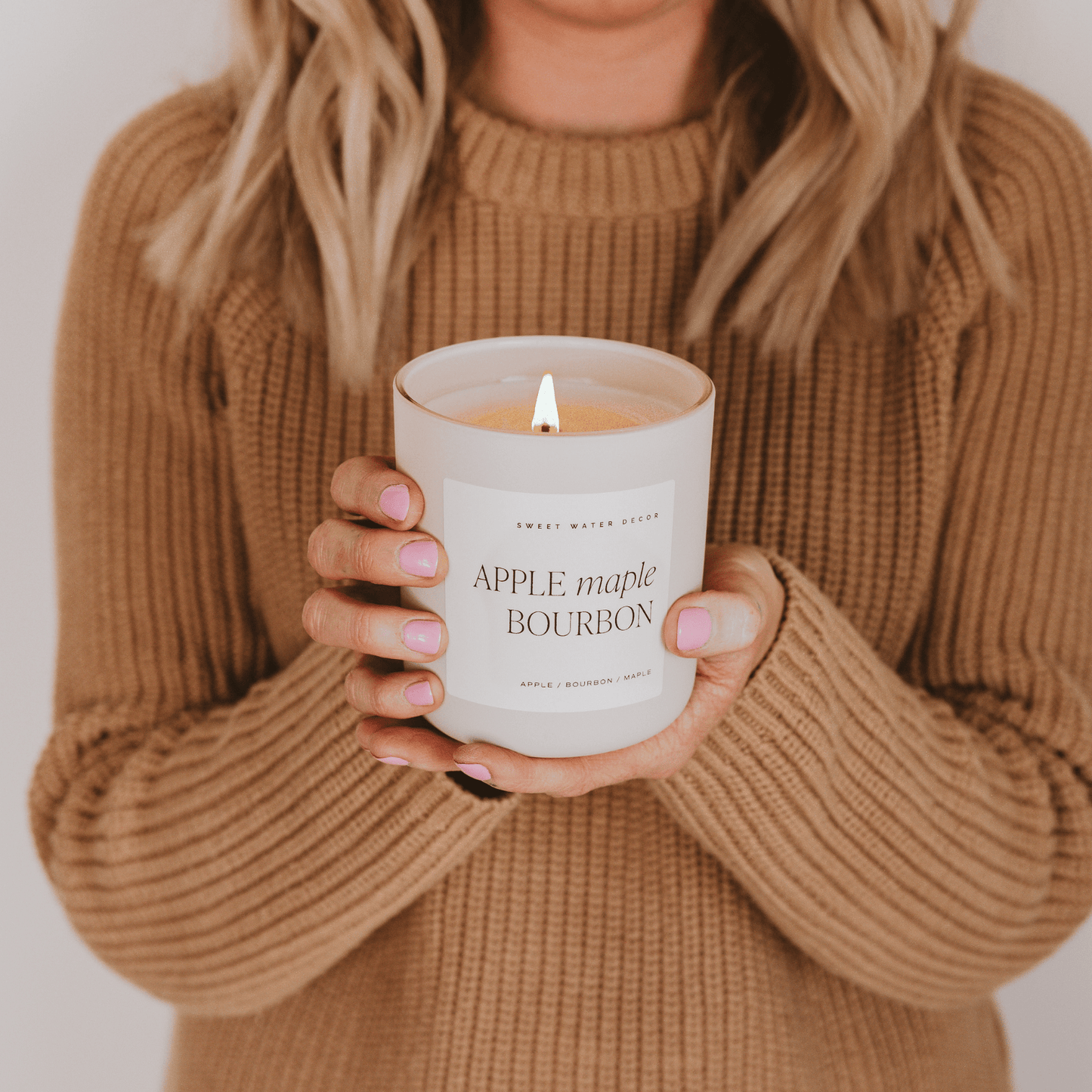 
                  
                    Person holding lit Apple Maple Bourbon 15 oz soy candle with wood lid in cozy fall setting
                  
                