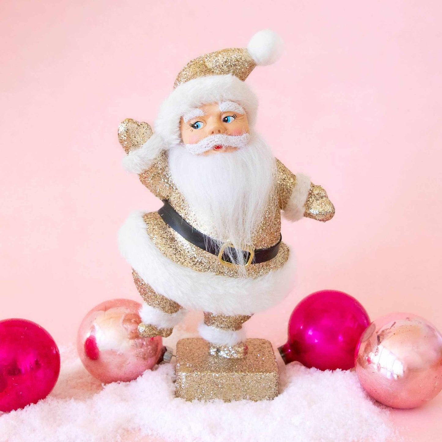 Retro flocked dancing Santa figurine in gold sparkle with fuzzy texture and playful pose on snowy surface with pink ornaments
