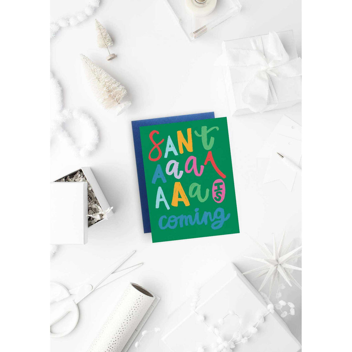 
                  
                    Santaaa Card holiday greeting card with colorful text on green background and pink envelope on festive white table setting
                  
                