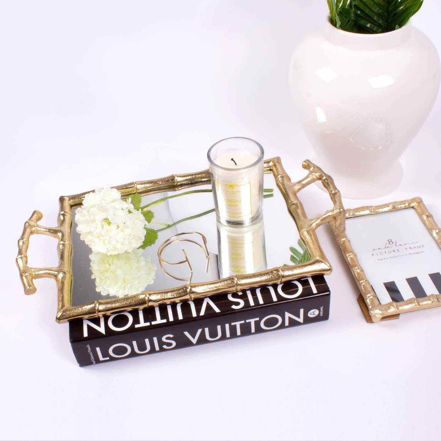 Gold bamboo framed mirrored vanity tray with candle, flower, and jewelry on luxury book display