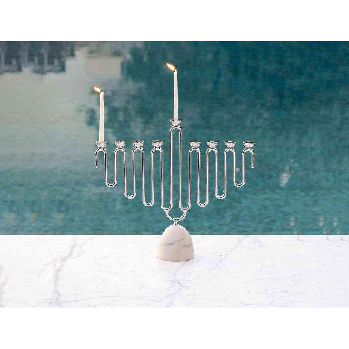 
                  
                    Coluna Menorah with Carrara Marble base and silver metal candle holders, modern design with burning white candles
                  
                