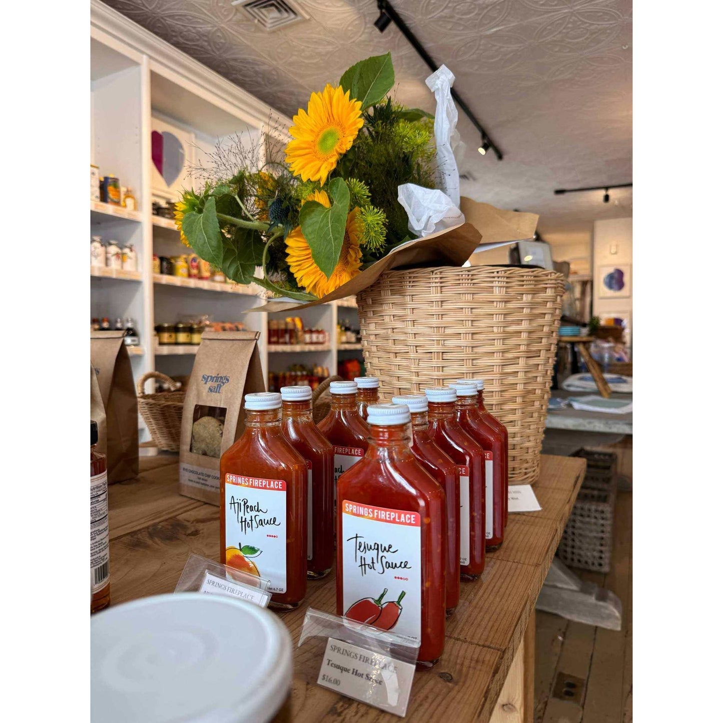 Aji Peach hot sauce bottles with sunflowers in a rustic store setting