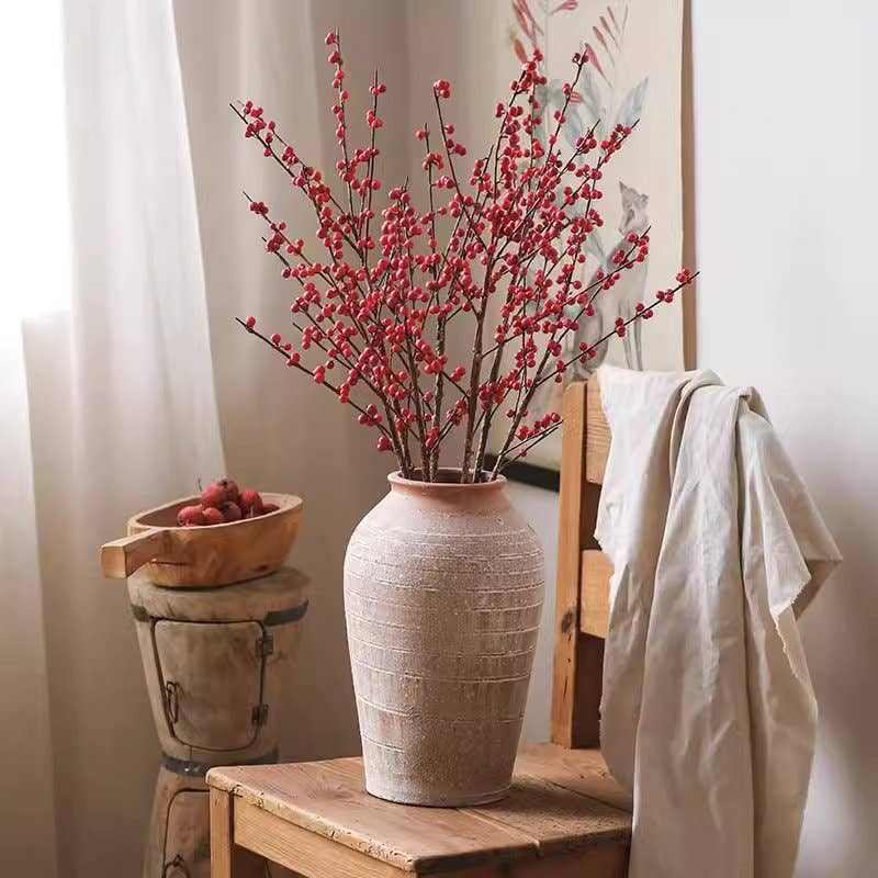 Faux red winterberry stem with vibrant artificial berries in a textured vase for seasonal home decor