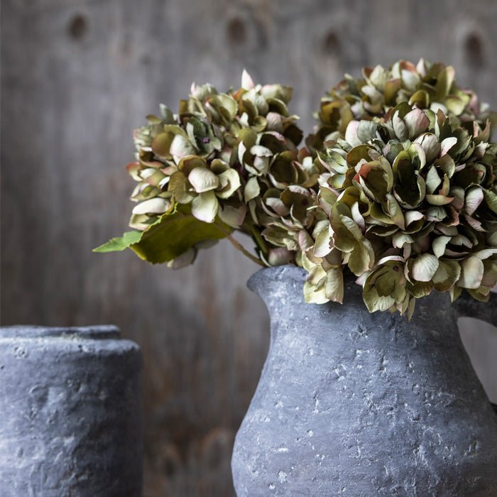 
                  
                    Abigail Ahern Real Touch Hydrangea Chloris stem in green with purple tinges, styled in a stone vase
                  
                