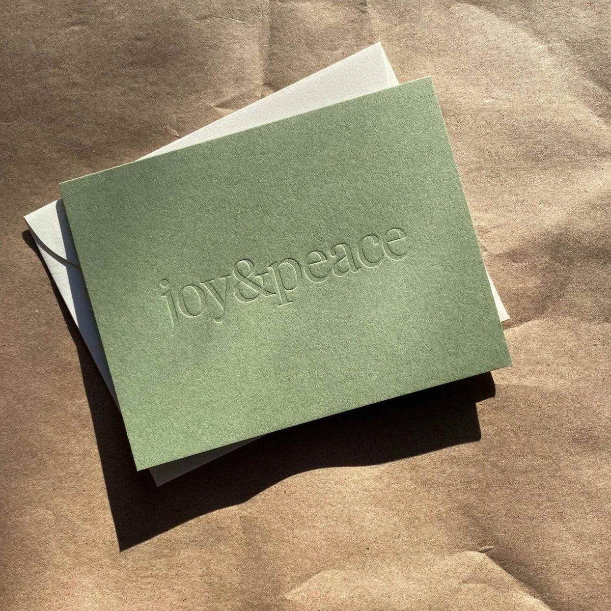 
                  
                    Joy & Peace No. 01 olive folded card with blind deboss and natural envelope on brown background
                  
                