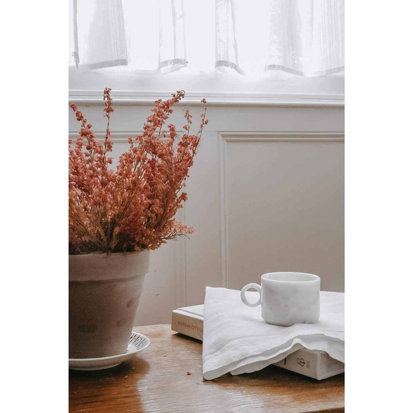 White marble tea cup on white cloth beside dried flowers in pot on wooden table