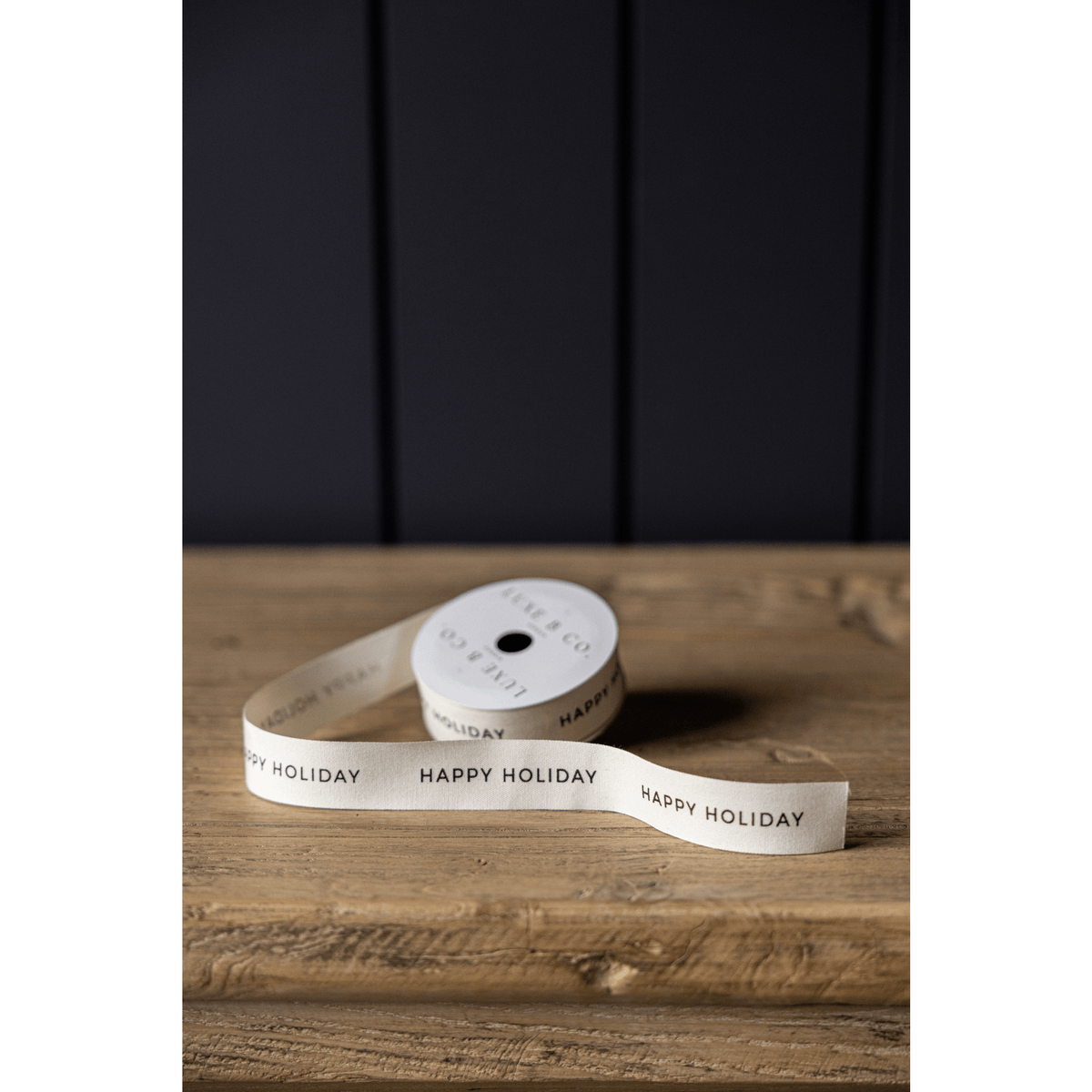 
                  
                    Happy Holiday Ribbon spool 1 inch wide with repeating "Happy Holiday" text on white satin ribbon for gift wrapping and packaging décor.
                  
                