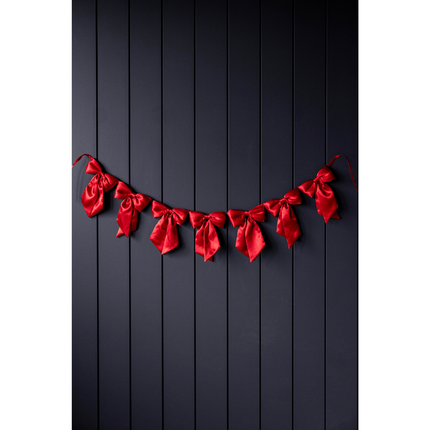 Red satin bow garland with seven soft fabric bows on dark background
