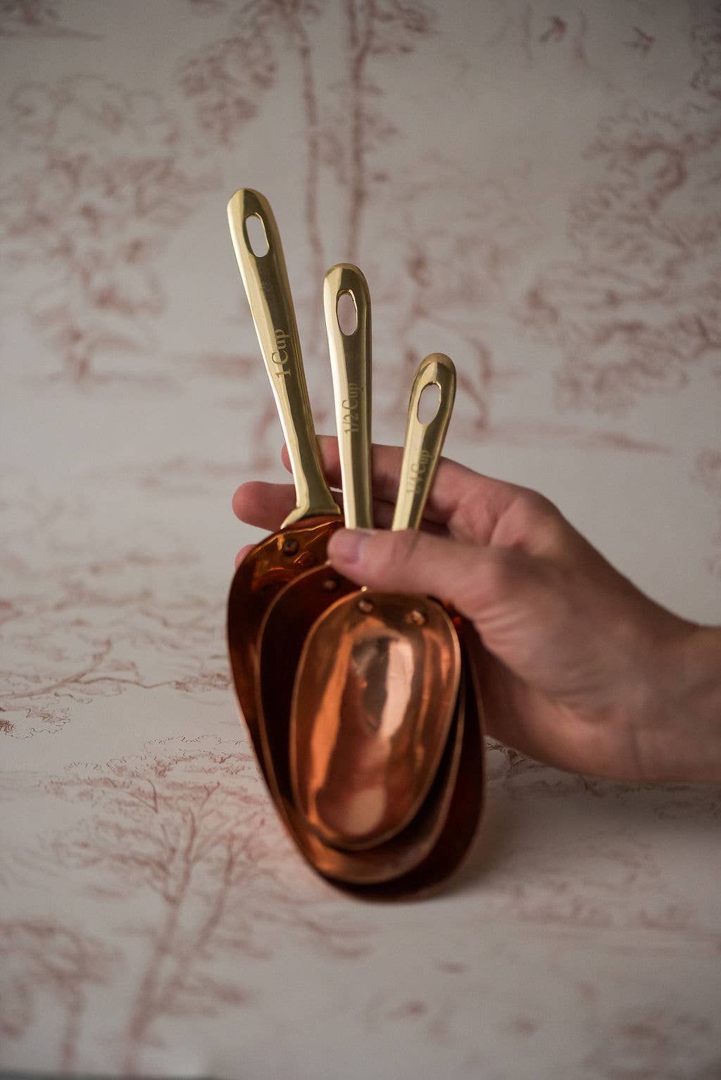 Set of 3 copper measuring scoops with brass handles held in hand for baking and cooking measurement.