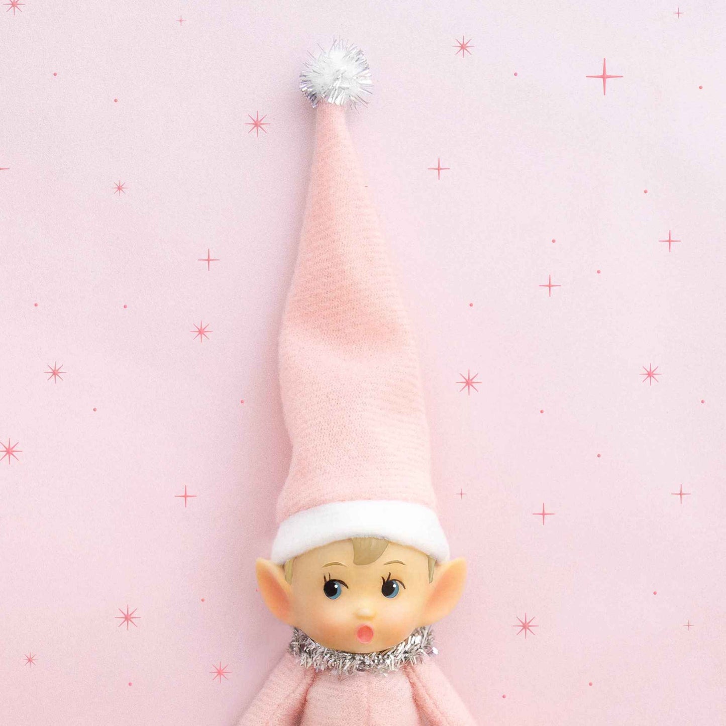 Elf Ornament Little Lou with pink hat and tinsel collar against pink star background