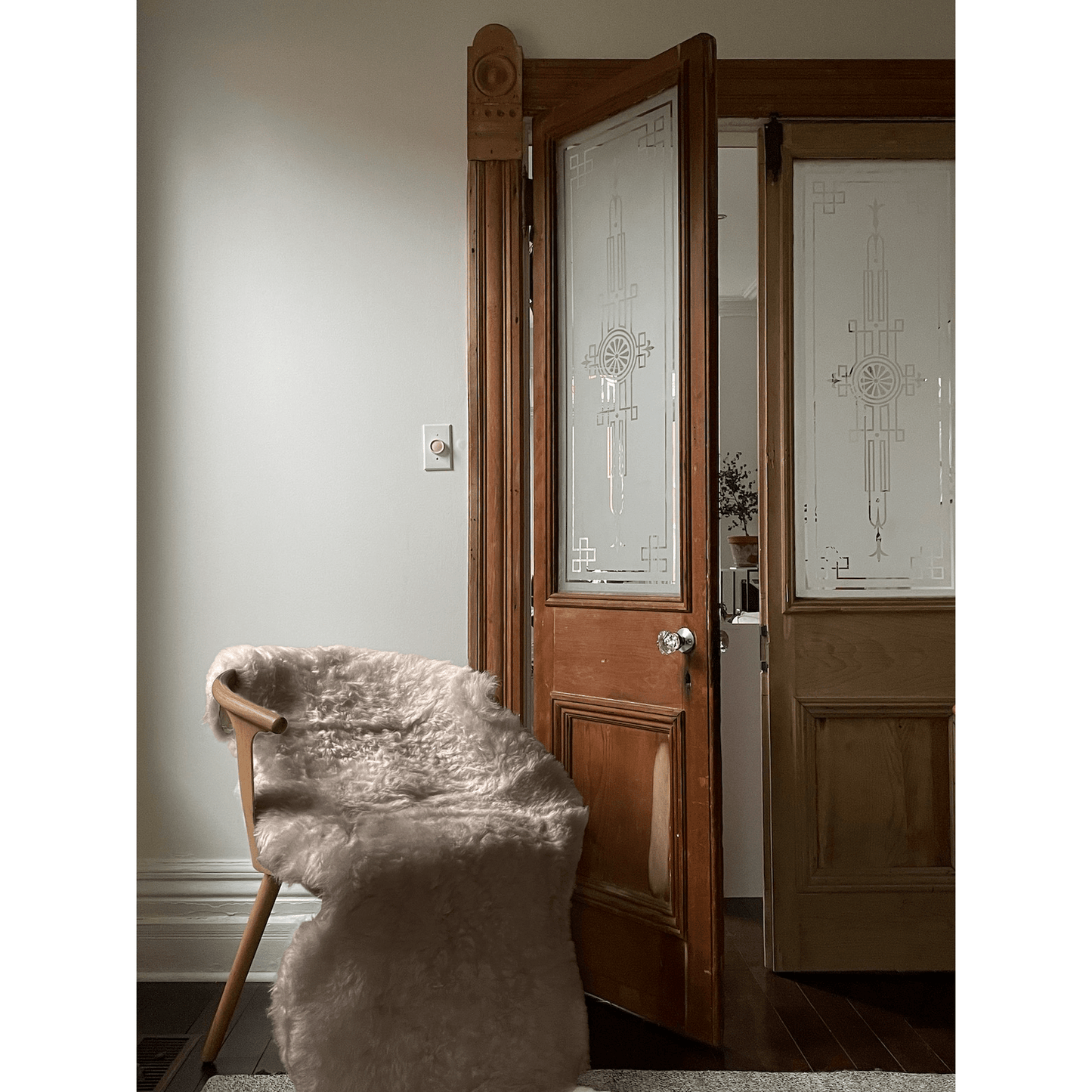 Shorn taupe double Icelandic sheepskin rug draped over chair in cozy room with wooden door