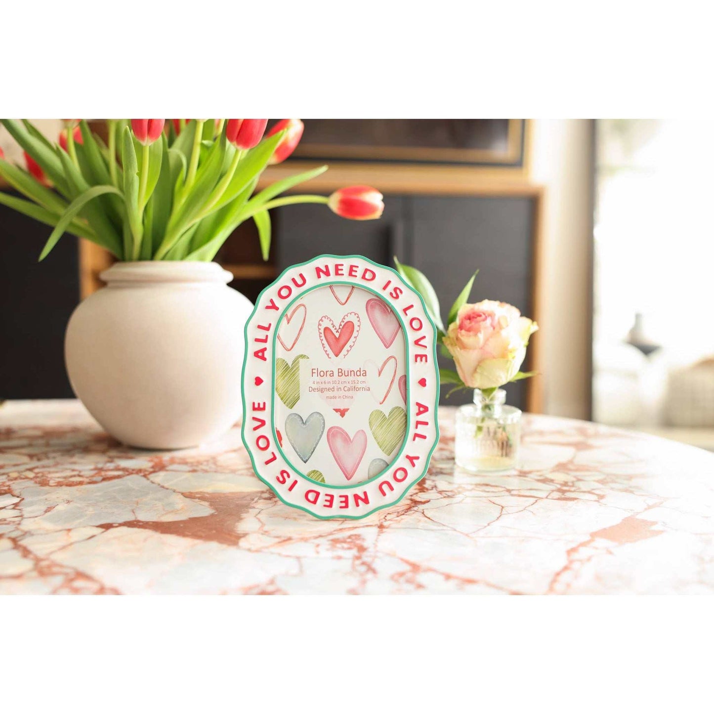 
                  
                    Ceramic heart photo frame with scalloped edges, colorful hearts, and raised All You Need Is Love lettering
                  
                
