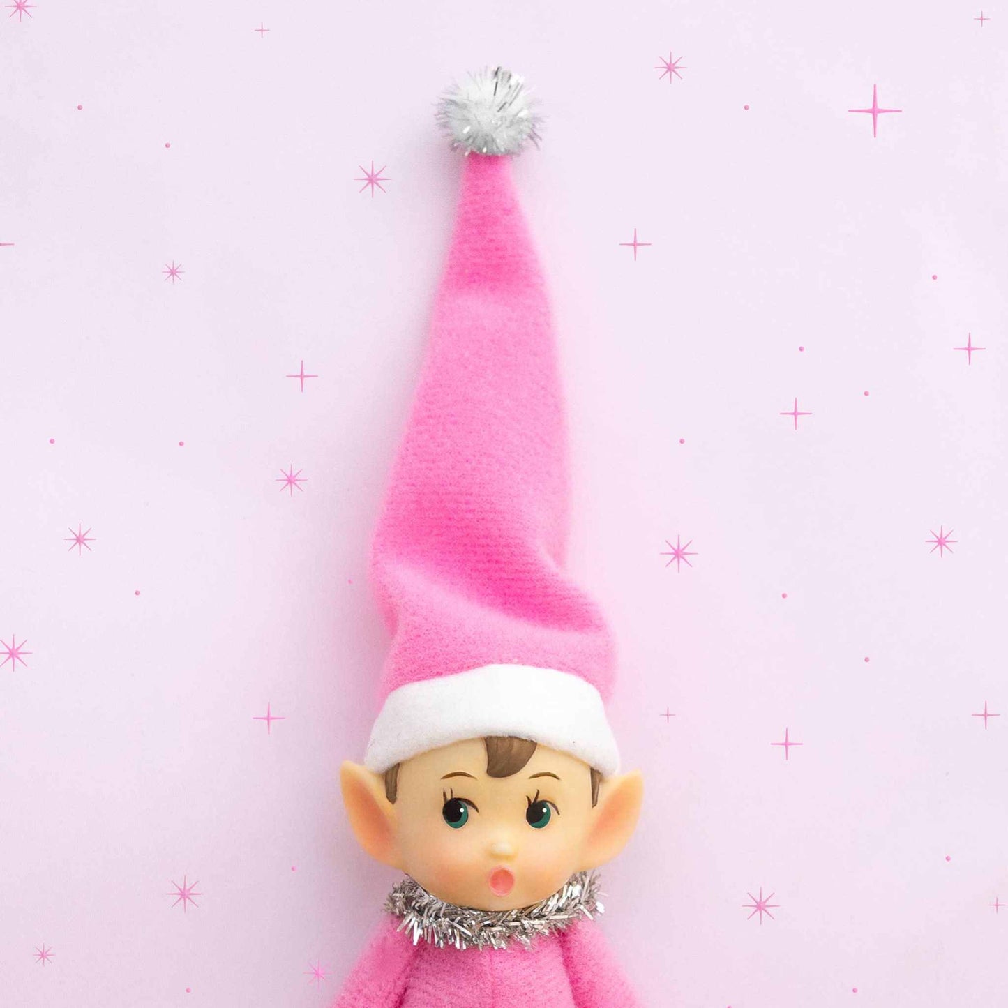 Pink felt elf ornament with bendable limbs and tinsel collar against light pink background