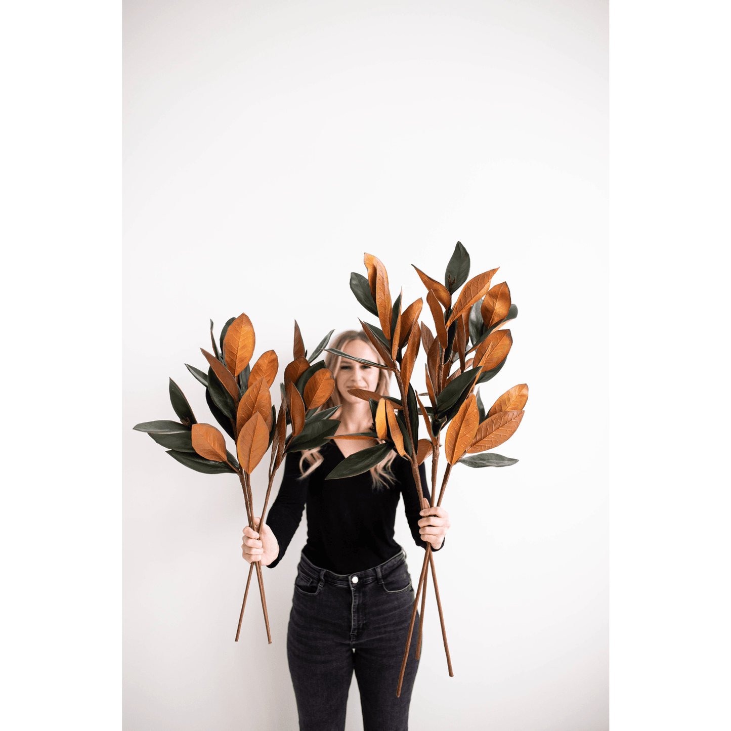 Woman holding small magnolia faux leaves in green and copper tones for home decor