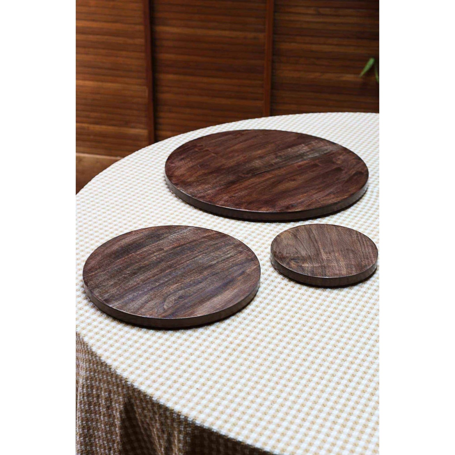 set of 3 round wooden serving boards made from dark mango wood with matte finish on checkered tablecloth