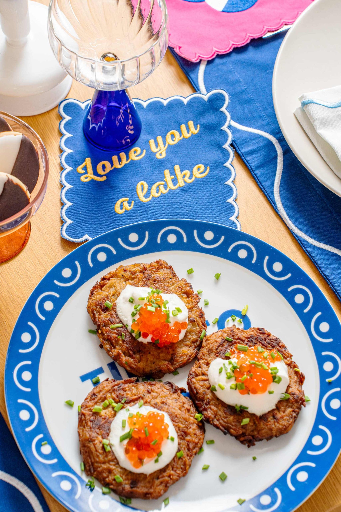 Embroidered blue napkin with "Love you a latke" phrase next to plate of latkes, Hanukkah Set table setting