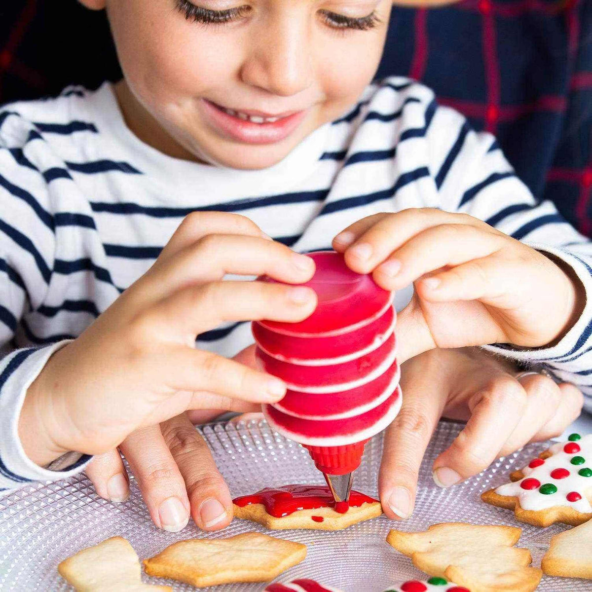 
                  
                    Child decorating Christmas cookies with red icing using Christmas Baking Set tools
                  
                
