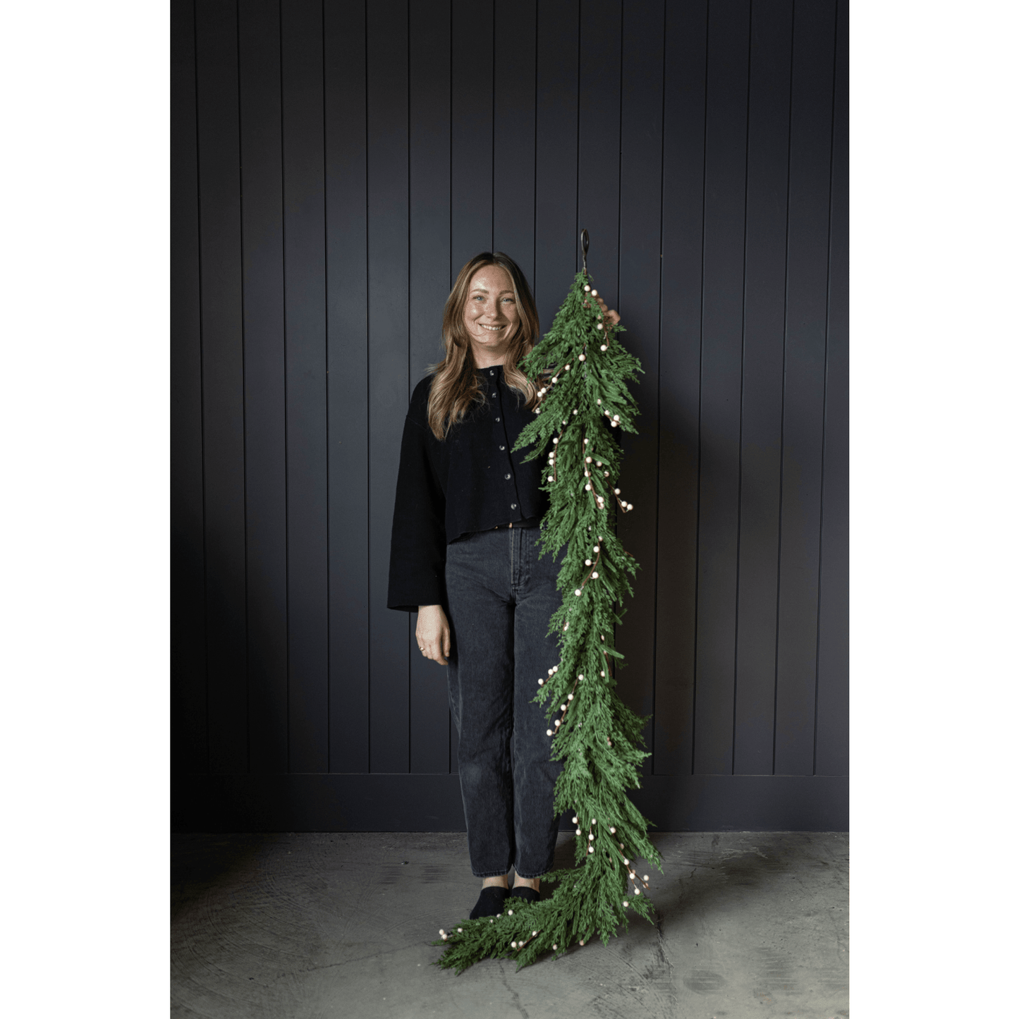 White Plum Berry Norfolk Cypress garland 6 ft with white berries held by smiling woman against dark wall