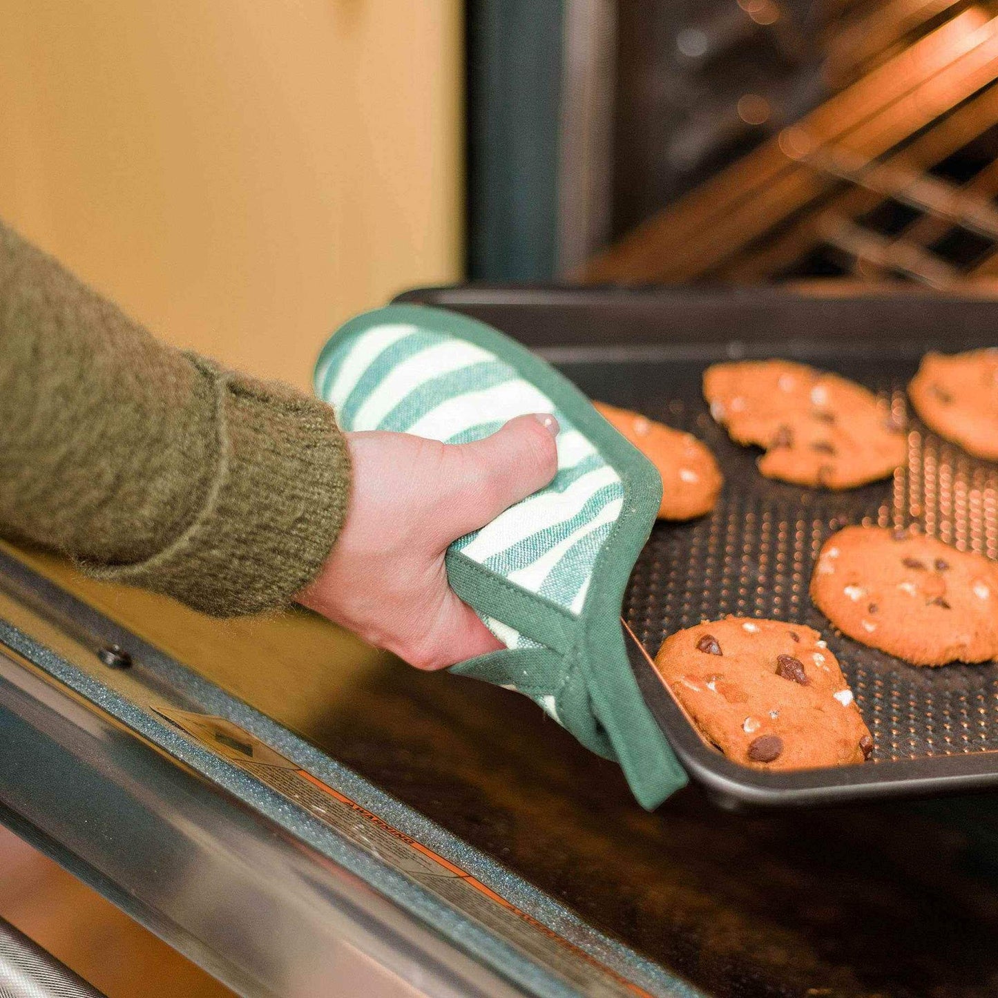 Hand using Holiday Floral Pot Holder Set to remove tray of cookies from oven
