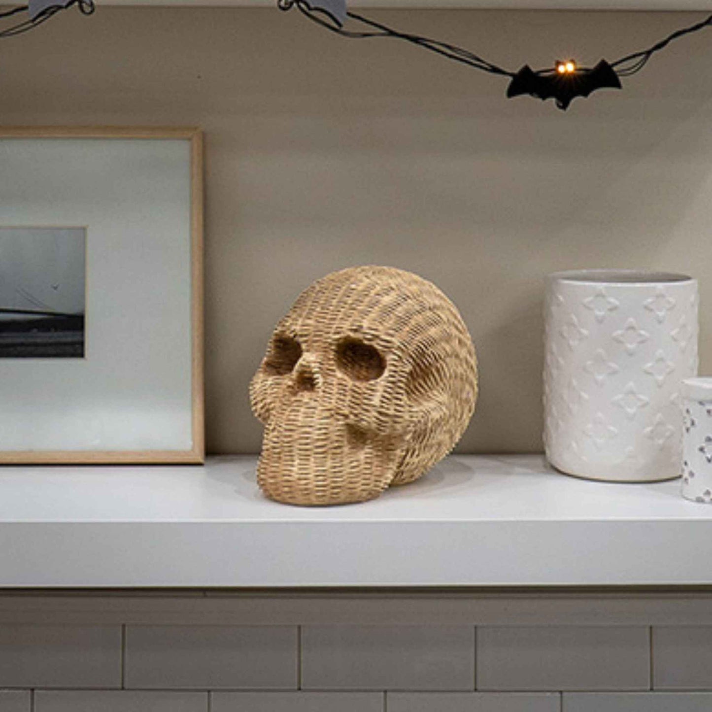 Wicker-look resin decorative skull in khaki with woven texture on shelf with Halloween bat lights