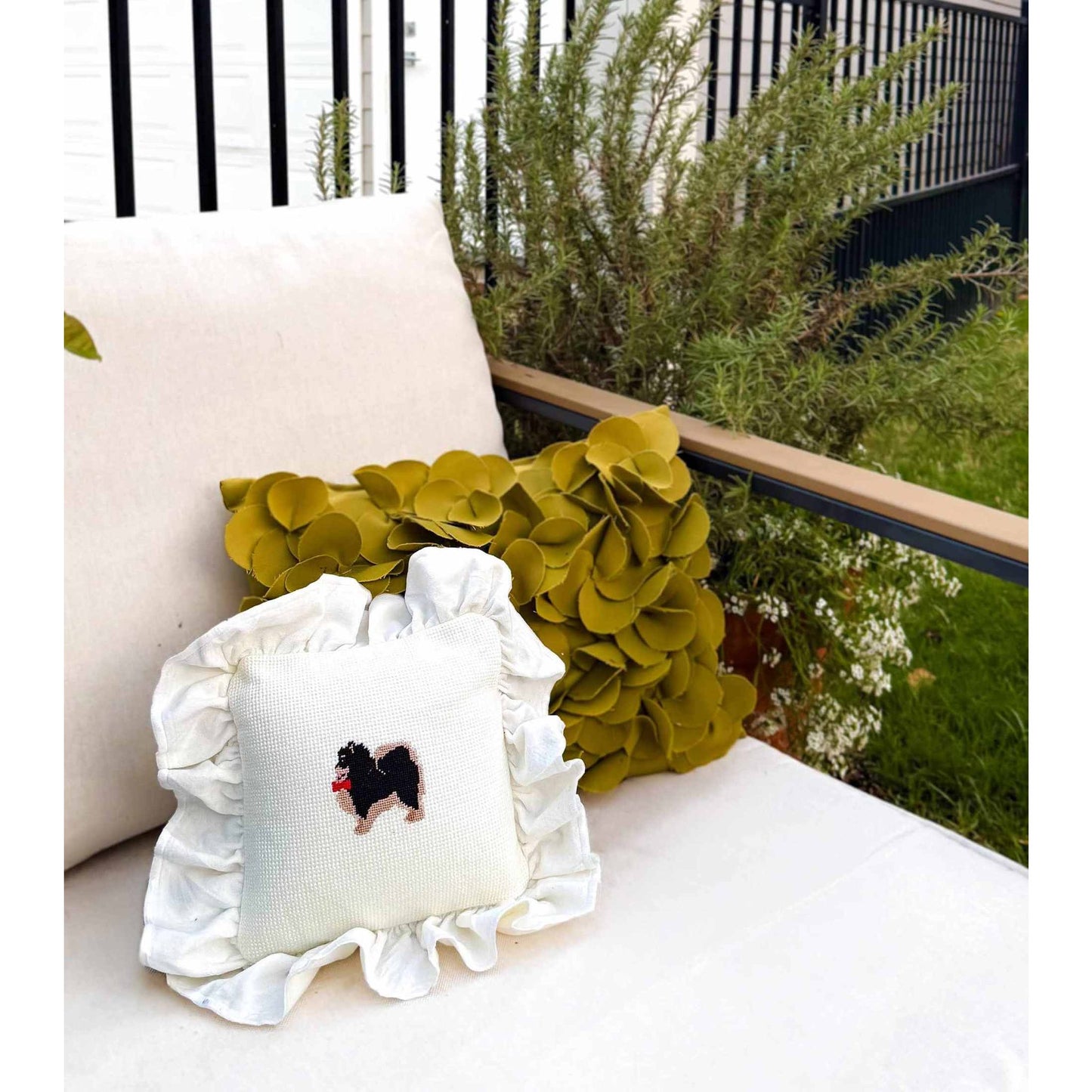 White Pomeranian Needlepoint Pillow with ruffled edges on outdoor sofa with green floral pillow