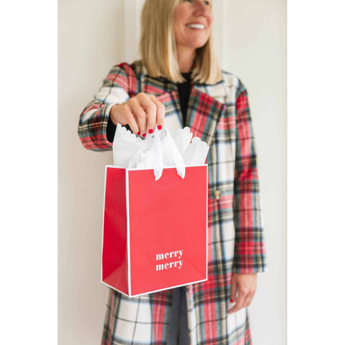Sugar Paper Merry Merry red gift bag with white grosgrain ribbon handles held by woman in plaid coat