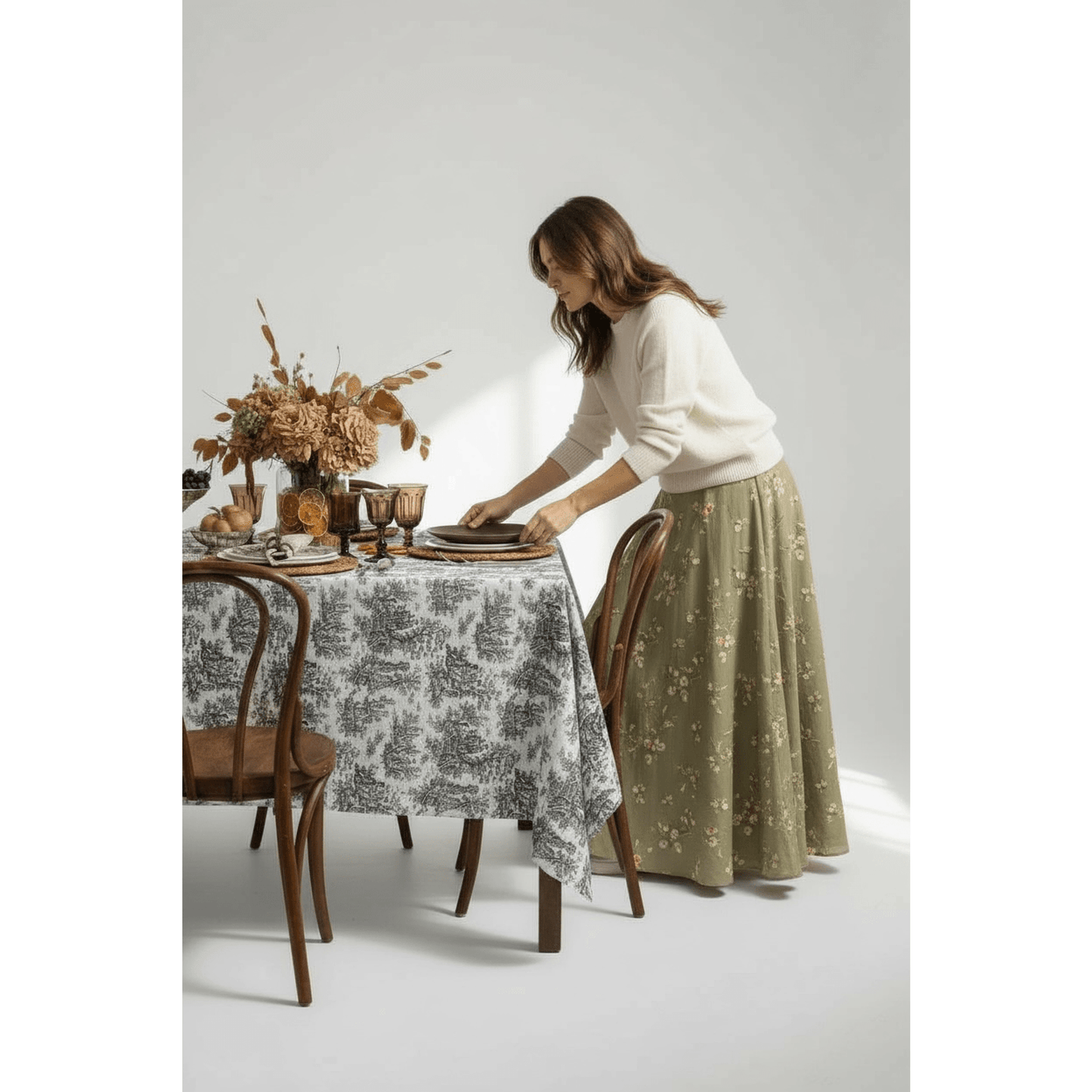 Oversized black and white botanical toile tablecloth on farmhouse table with rustic dining setup and woman arranging plates
