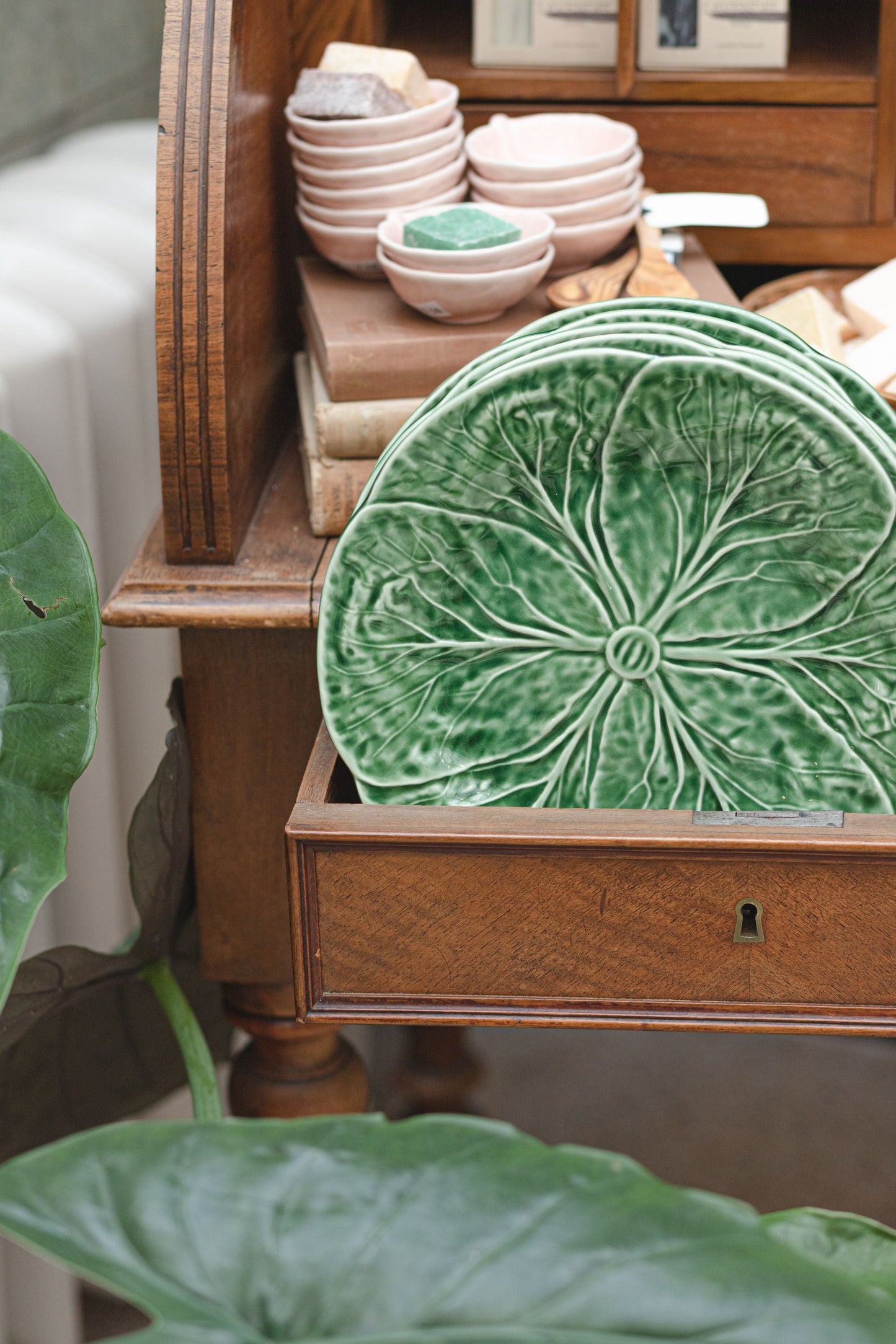 Green cabbage leaf plates displayed in a wooden drawer with pink ceramic bowls in the background