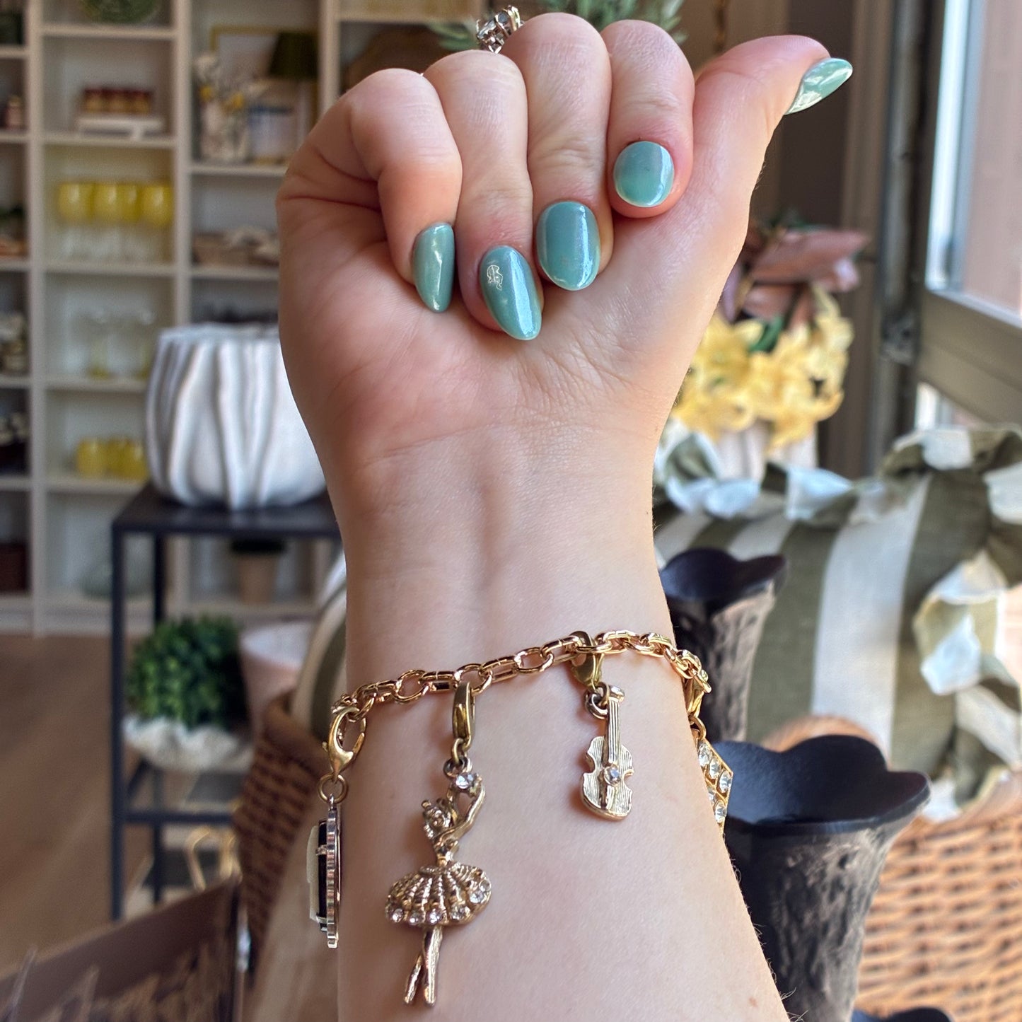 
                  
                    A close-up of a person's wrist wearing a gold-tone charm bracelet with a ballerina, guitar, and other charms
                  
                