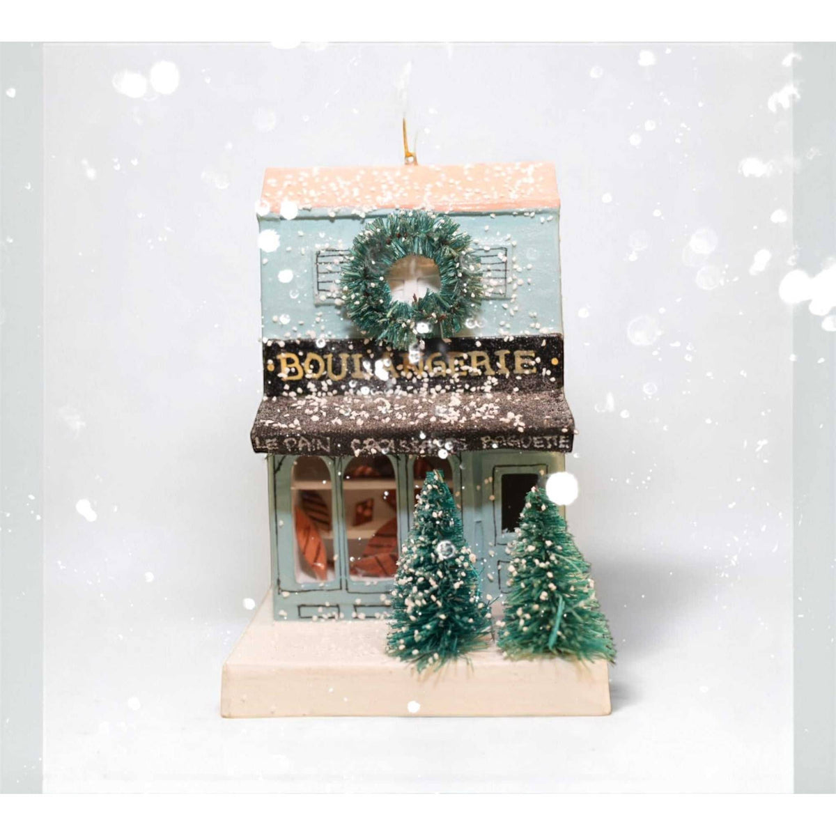 
                  
                    European Village Shop Boulangerie paper ornament with wreath and miniature trees in snow
                  
                