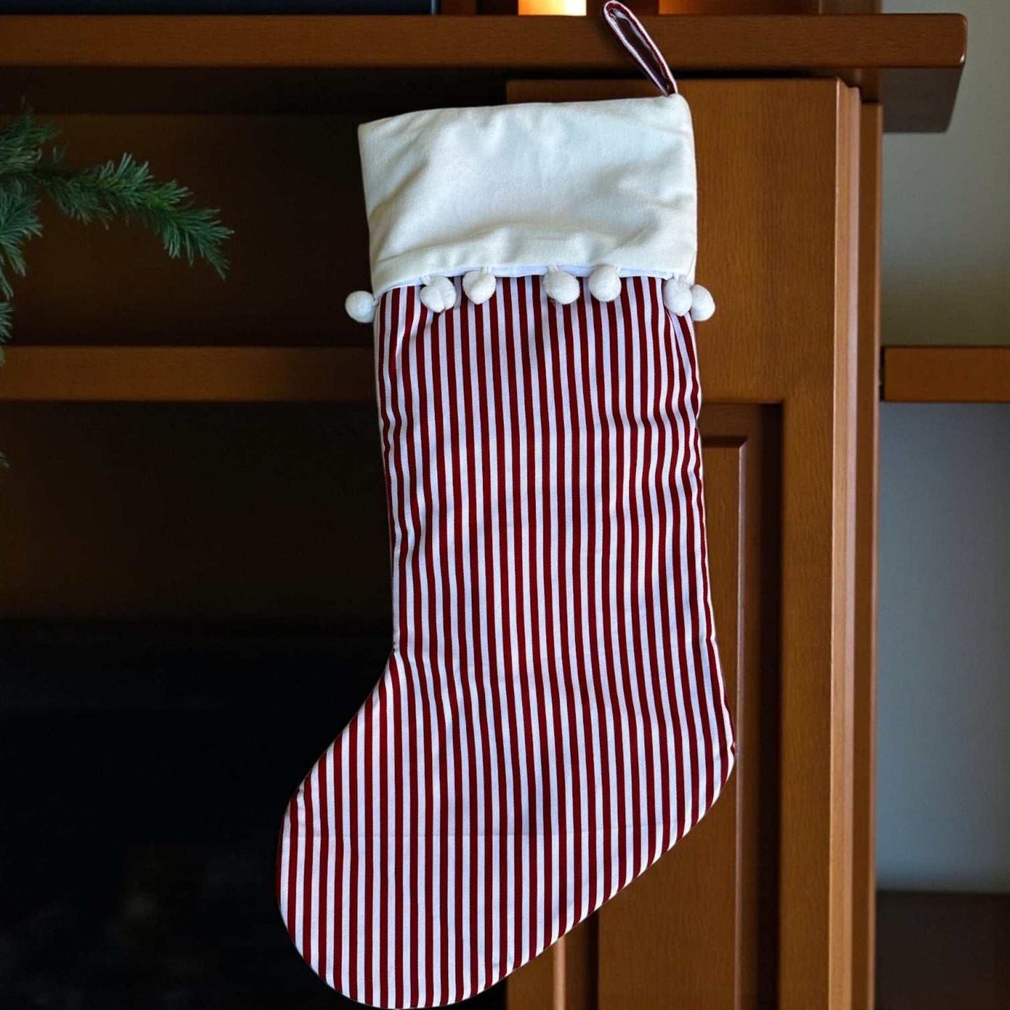Red and white stripe stocking with velvet cuff and pom poms hanging on a wooden mantel