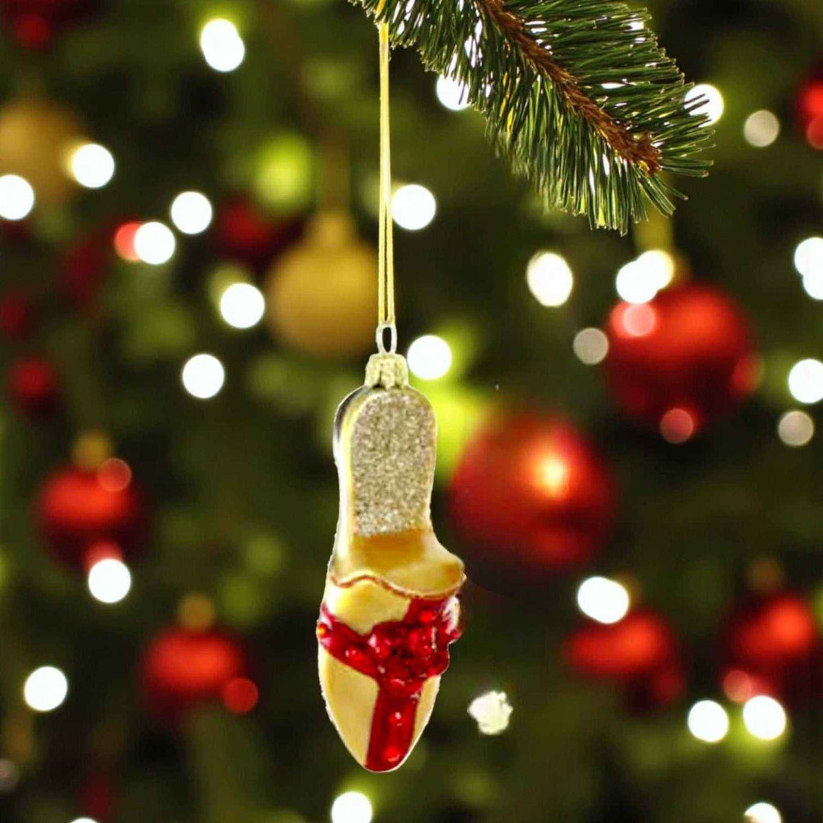 
                  
                    All Wrapped Up Shoes Christmas slipper ornament hanging on tree with festive lights background
                  
                