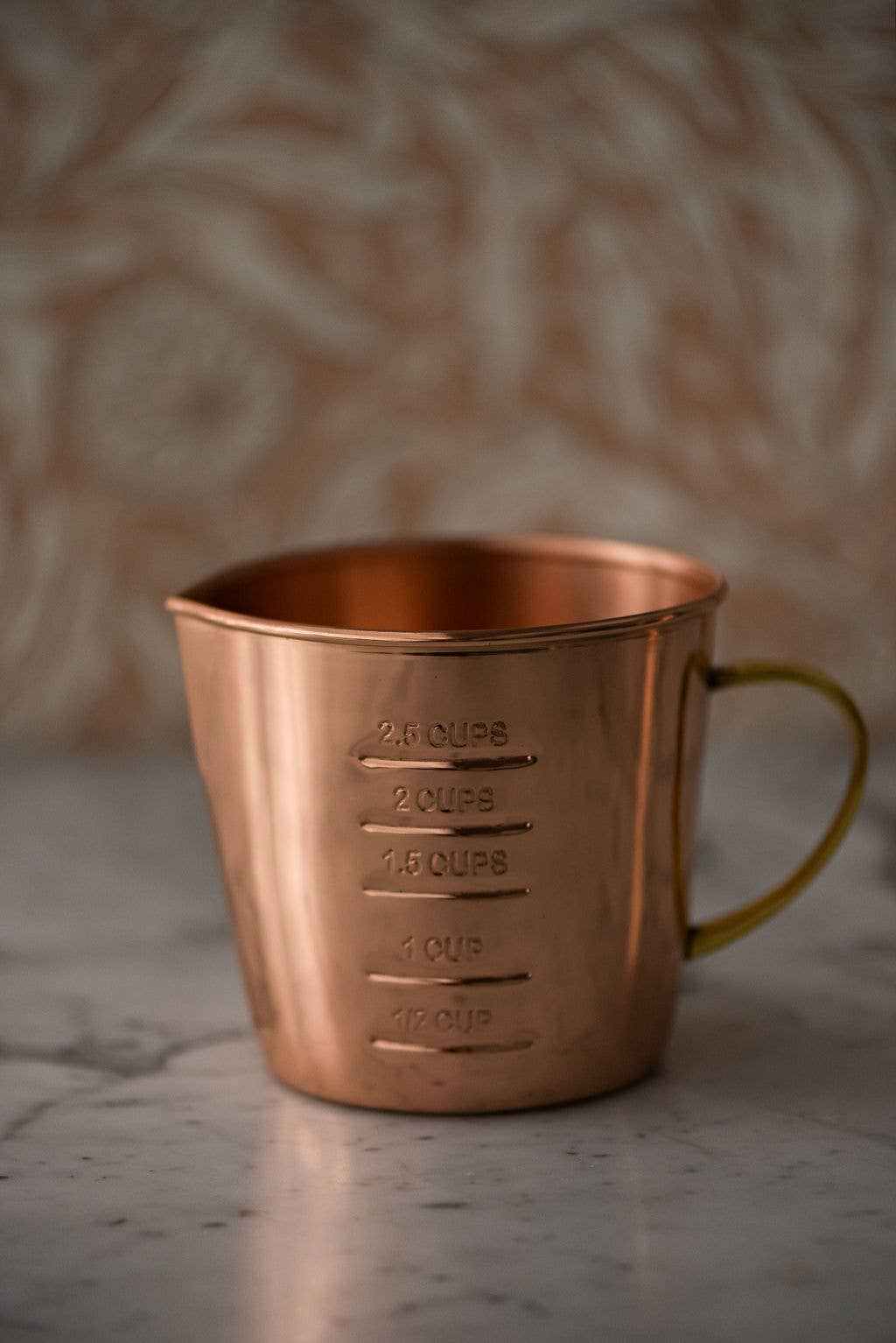 Copper liquid measuring cup with brass handle and 2.5 cup capacity showing interior and exterior measurement markings