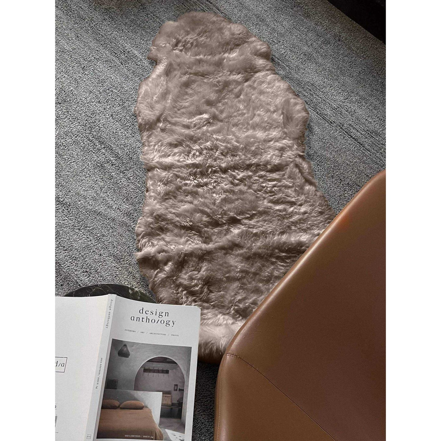 Shorn taupe double Icelandic sheepskin rug with soft long wool on floor next to chair and book