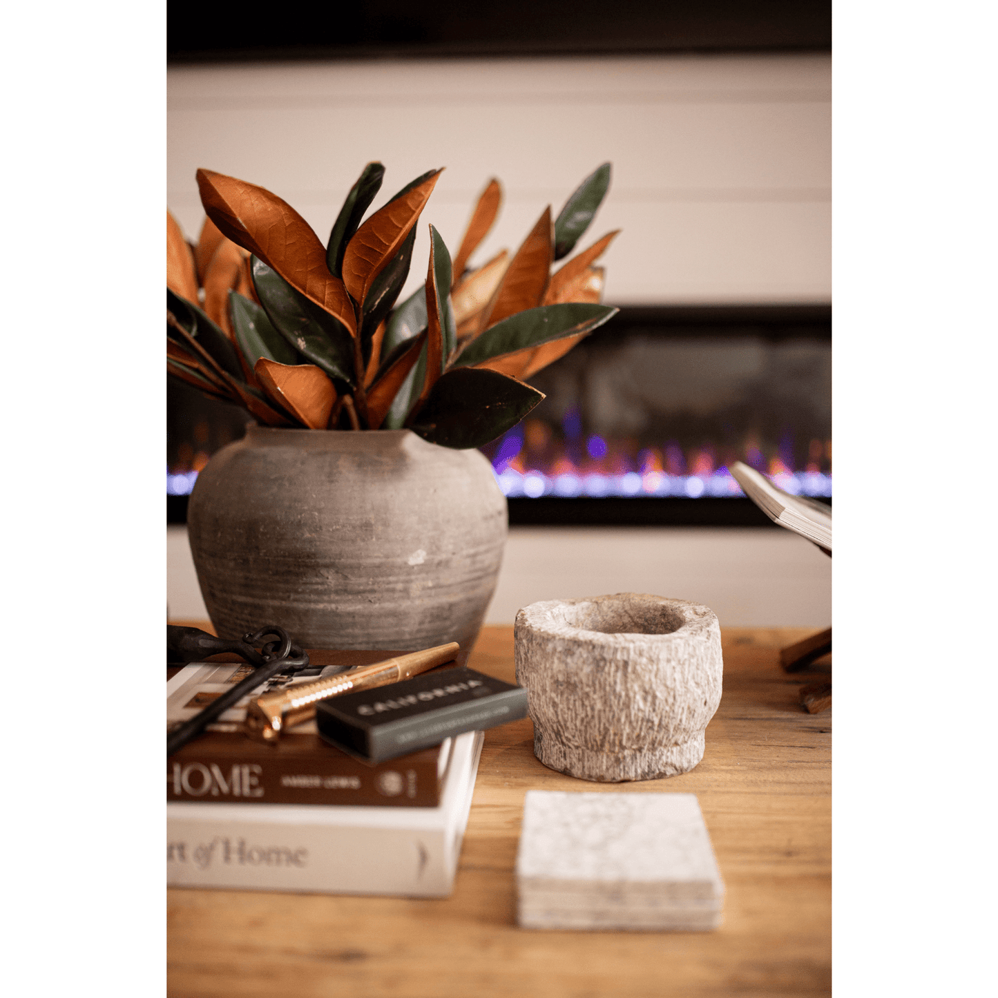 Large Magnolia Faux Leaves arrangement in grey vase on wooden table by fireplace
