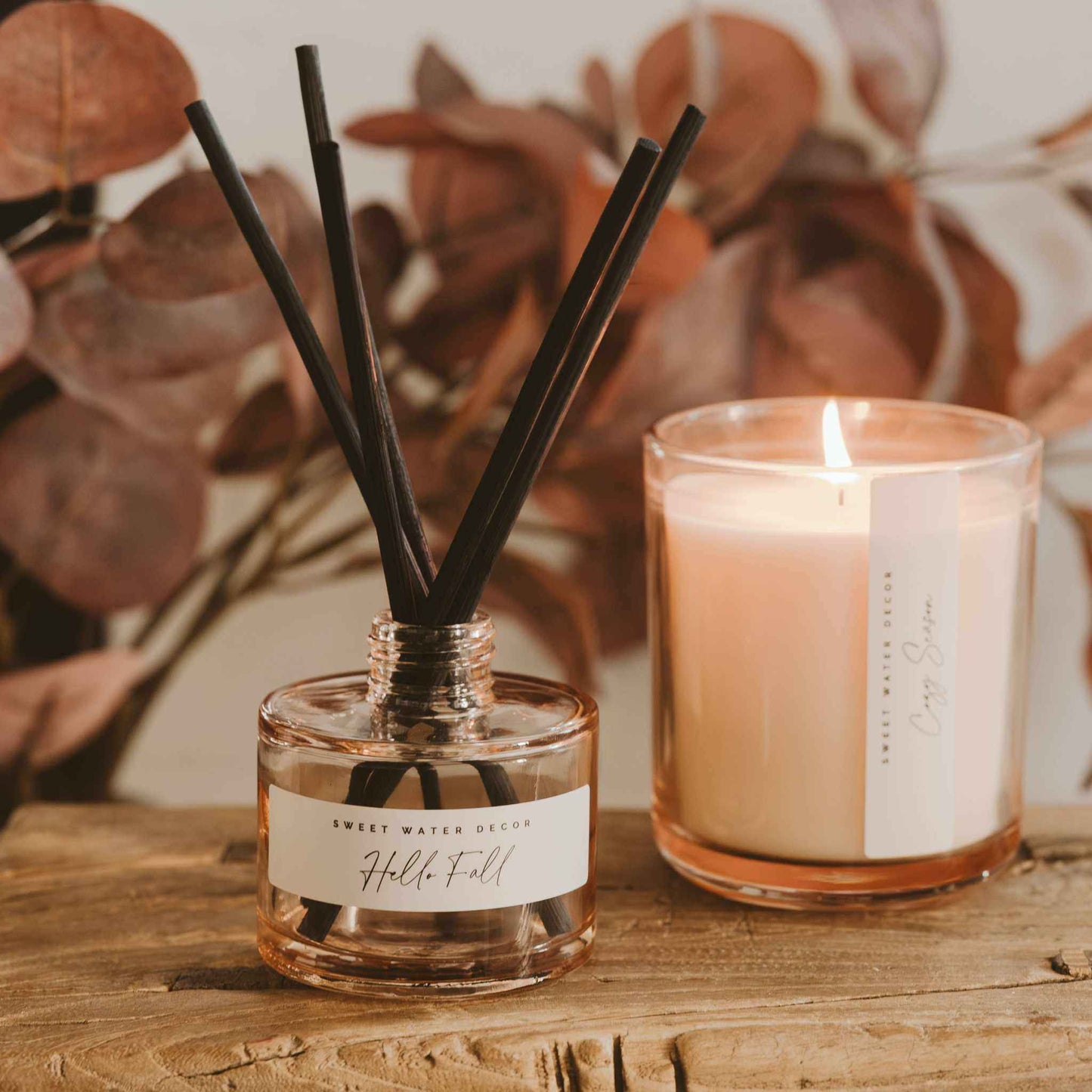 Hello Fall reed diffuser with black reeds in beige glass jar, autumn scent with cider, cinnamon, apple, and nutmeg notes, styled with fall decor and candle