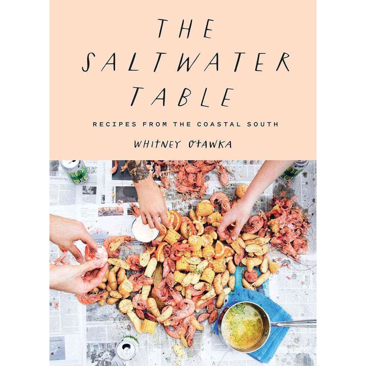 Saltwater Table cookbook cover with seafood boil spread on newspaper and hands peeling shrimp