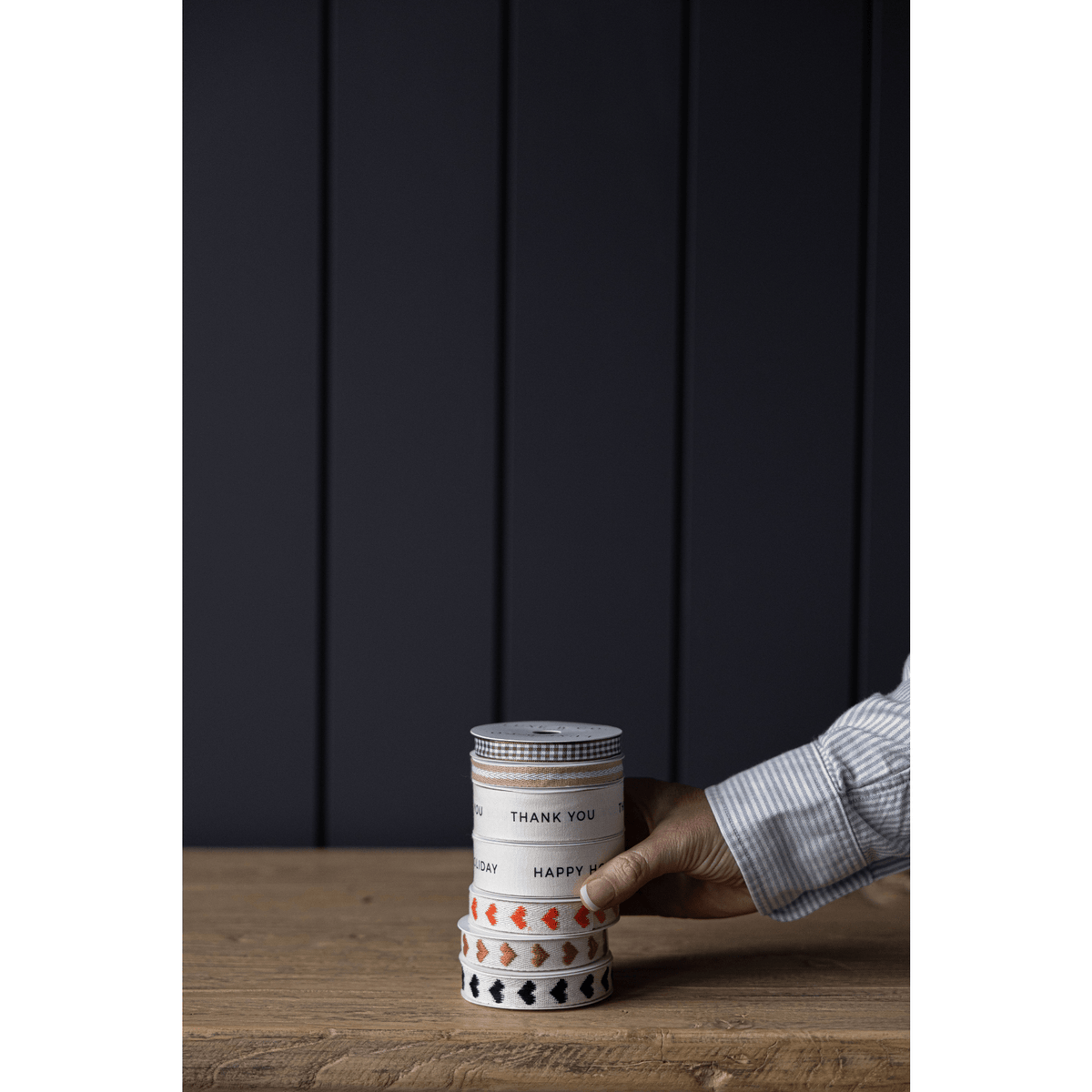 
                  
                    Spool of Happy Holiday Ribbon with thoughtful packaging accents on wooden table
                  
                