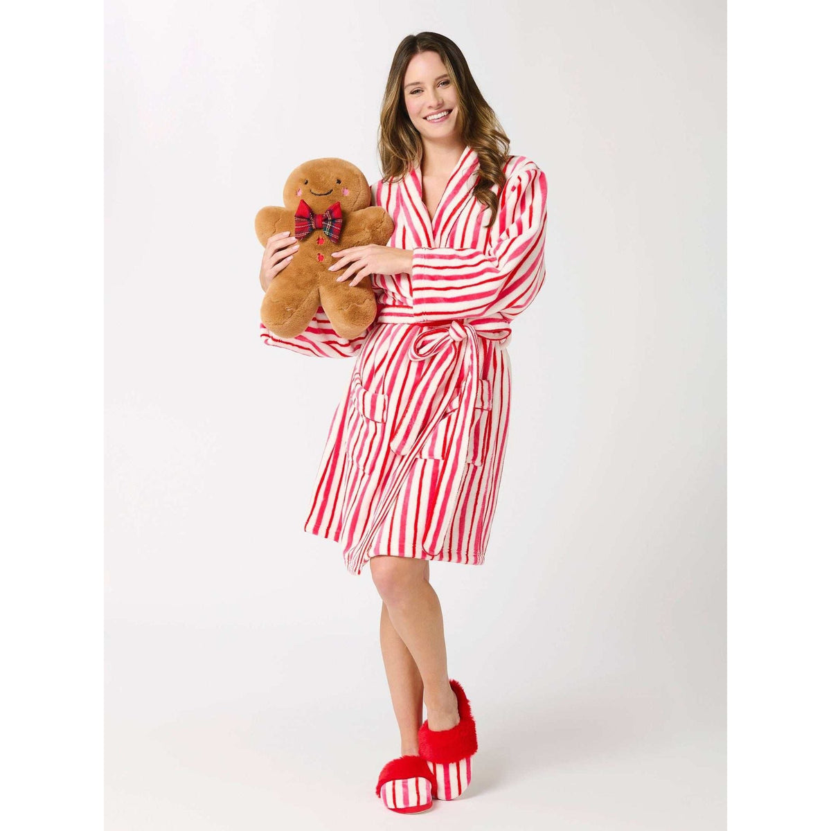 
                  
                    Woman in striped robe holding a plush Gingerbread Man Pillow with tartan bowtie and stitched details
                  
                