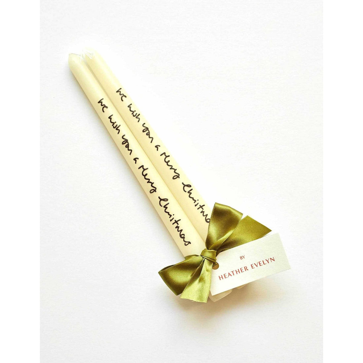 Pair of cream candles with "We wish you a merry Christmas" text tied with green ribbon