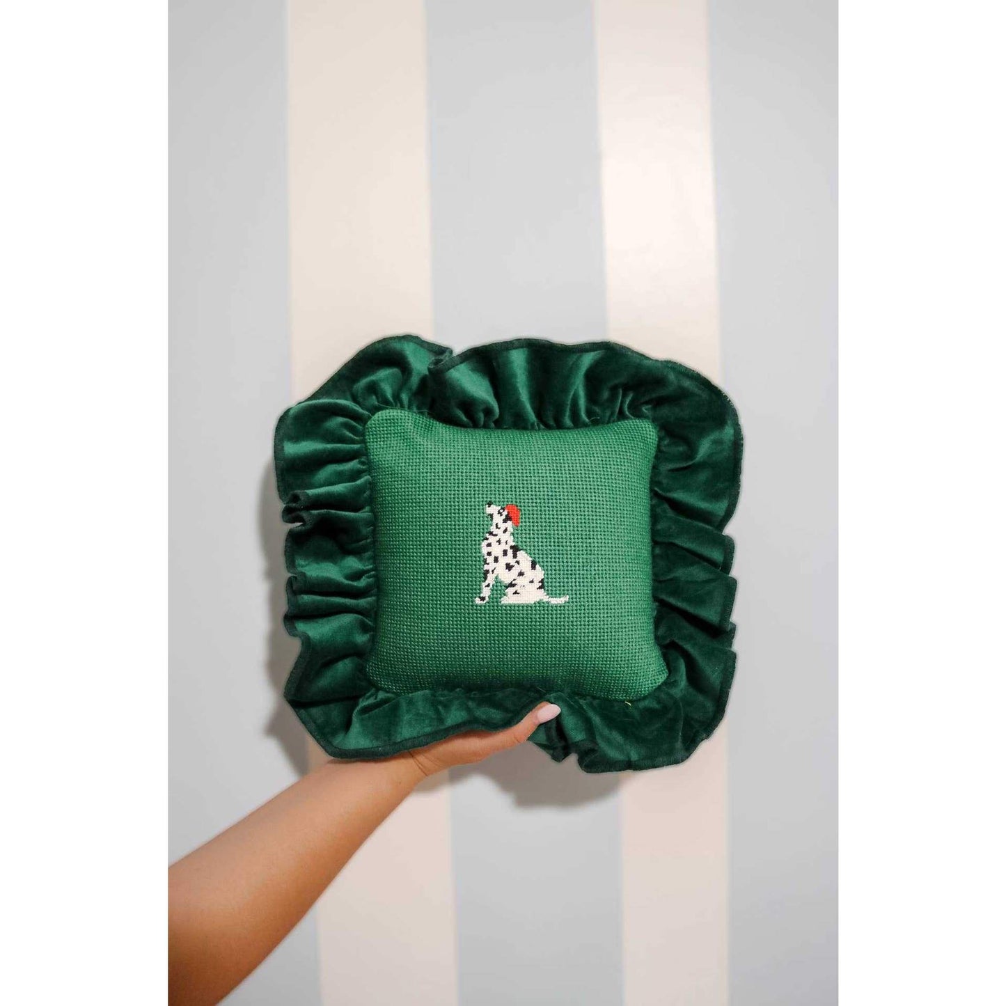 Green Dalmatian needlepoint pillow with velvet ruffled edges held against striped wall background