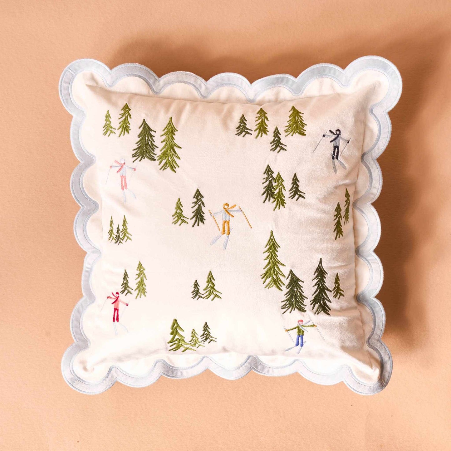 Scalloped square throw pillow with embroidered skiers and pine trees on cream background