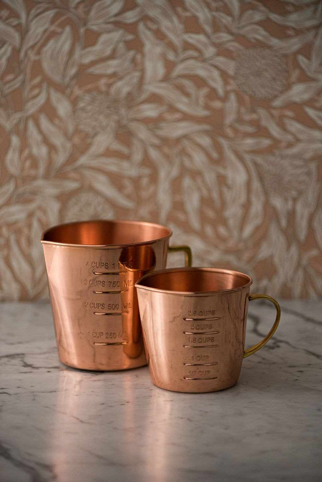 Copper liquid measuring cup with brass handle and clear interior and exterior markings on marble surface