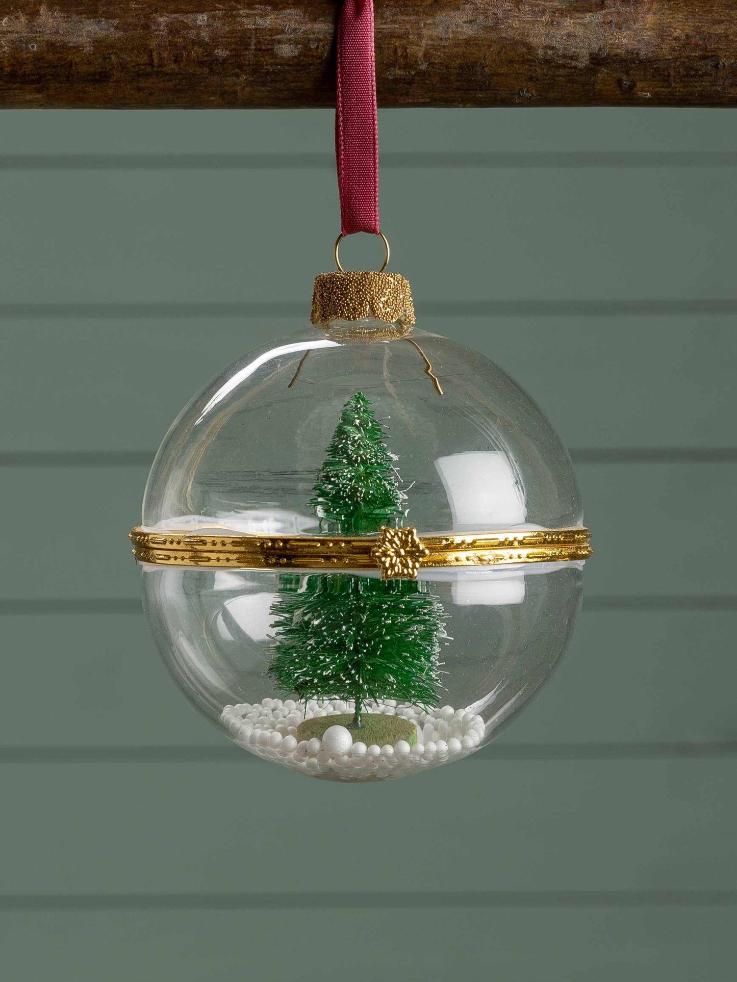 Round glass ornament with mini Christmas tree and faux snow inside hanging by red ribbon