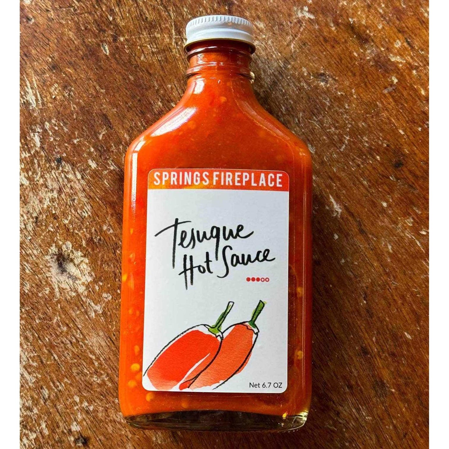 Bottle of Tesuque hot sauce with red chili pepper label on wooden surface