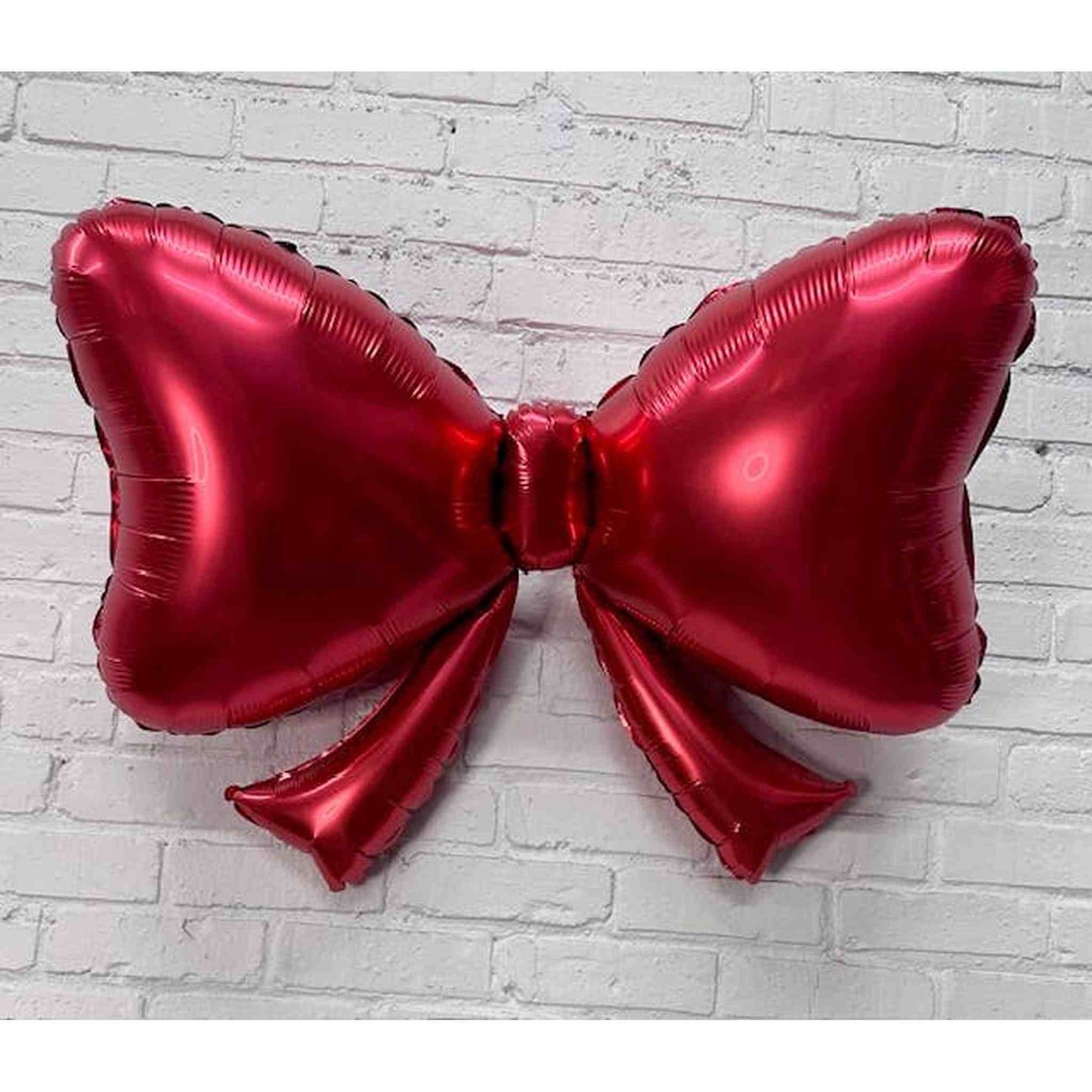Red Bow Balloon 40 inch shiny foil balloon shaped like a bow on white brick wall background