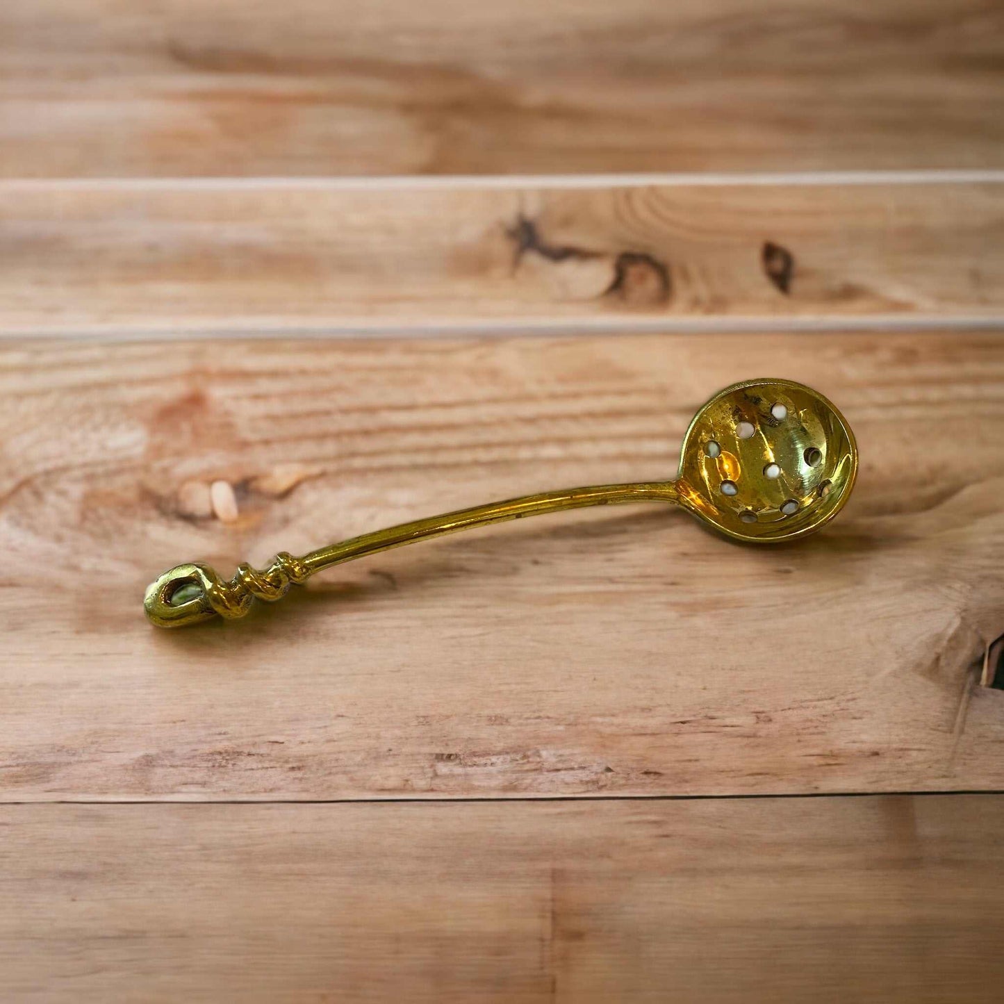 Brass ladle with holes on wooden surface for kitchen use