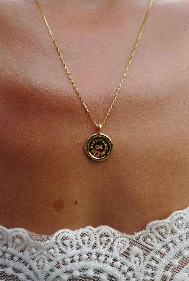 Gold plated Everything Will Be OK Charm on a delicate box chain necklace worn on neck with lace top background