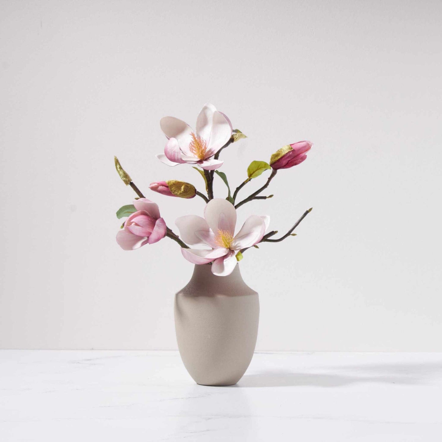 Magnolia blossoms arranged in a neutral metal Milan vase with soft pink flowers and green leaves