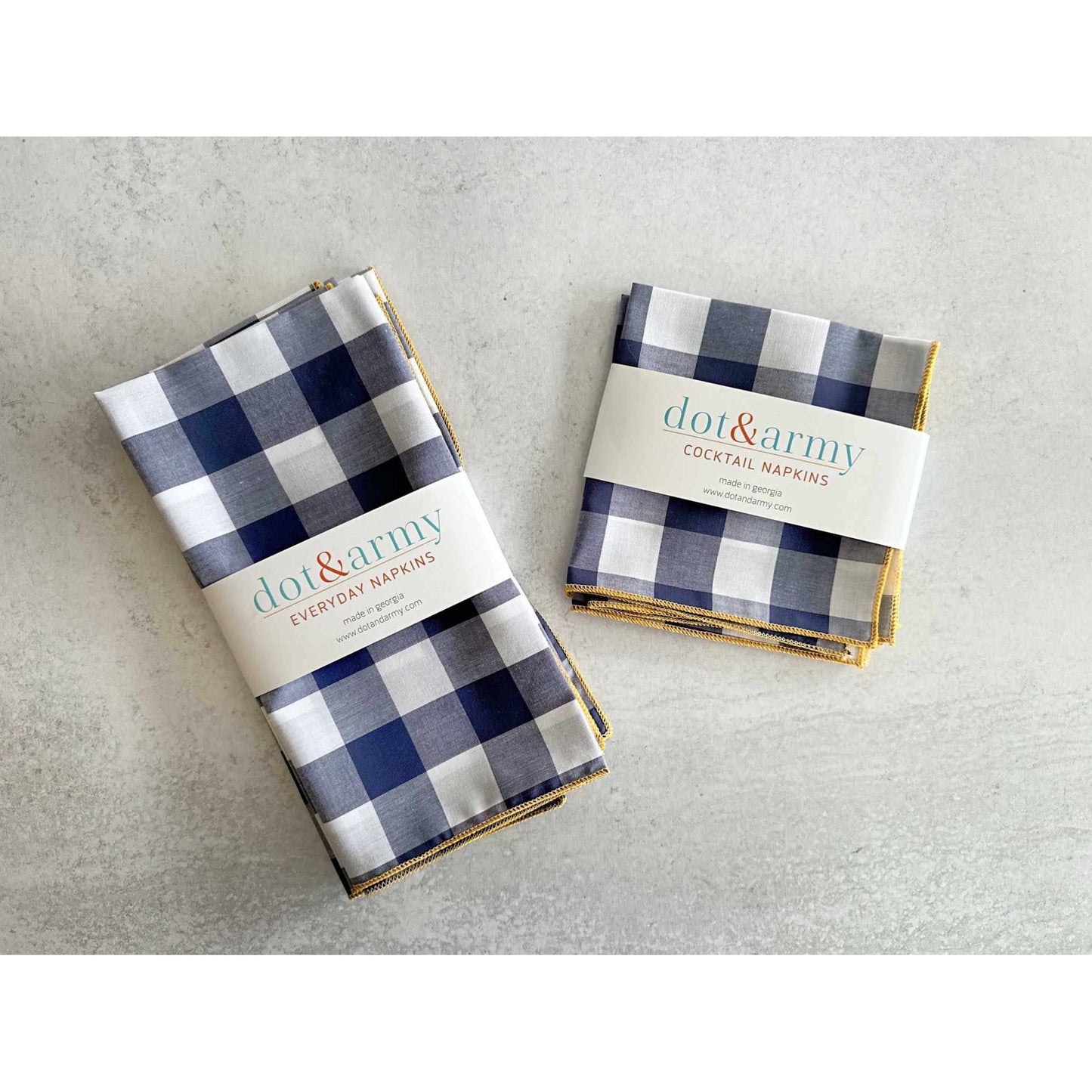 Set of four navy and white gingham check cloth napkins with honey mustard edging on a gray background